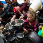 FILE PHOTO: Palestinian children wait to receive food cooked by a charity kitchen amid shortages of food supplies, in Rafah